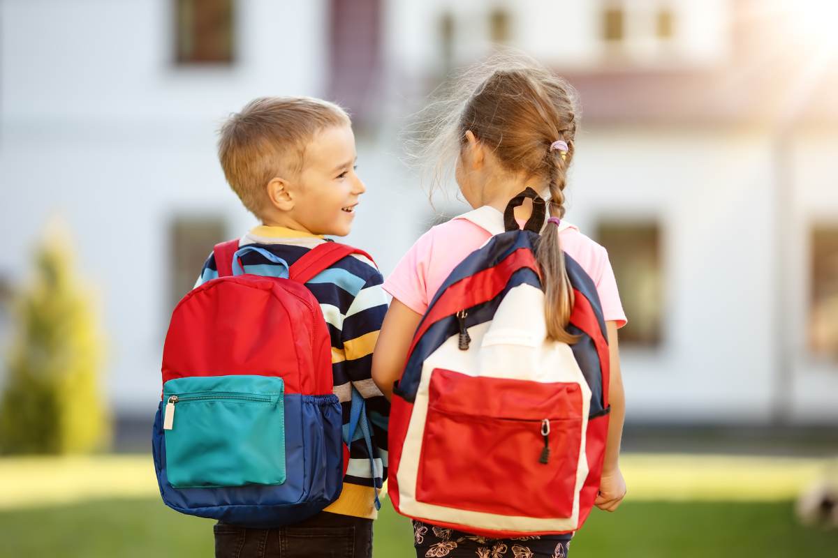 bambino e bambina vanno a scuola con zaino sulle spalle