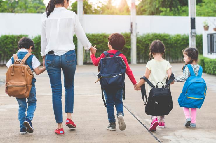 donna porta a scuola bambini con zaino in spalle